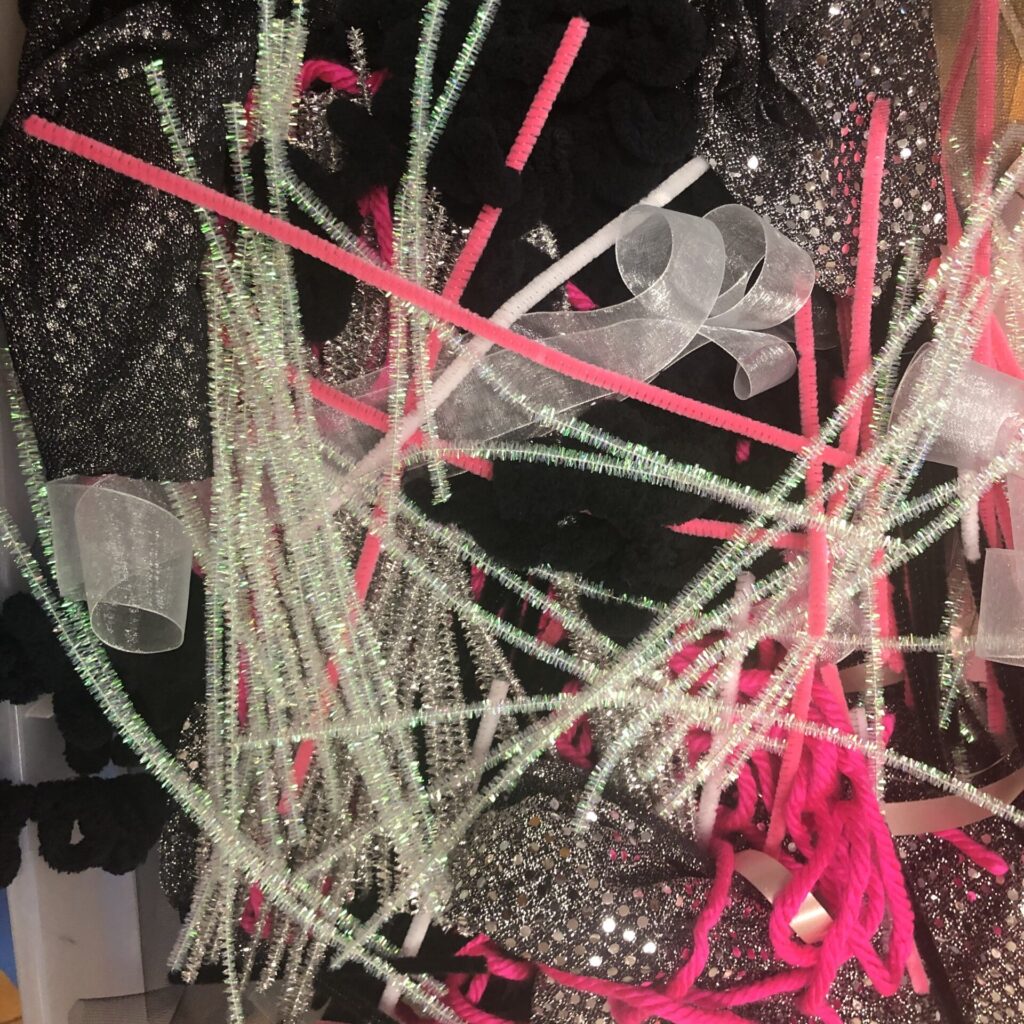 Mix of iridescent and neon pink pipe-cleaners, white ribbon, and black and silver sparkly fabric.