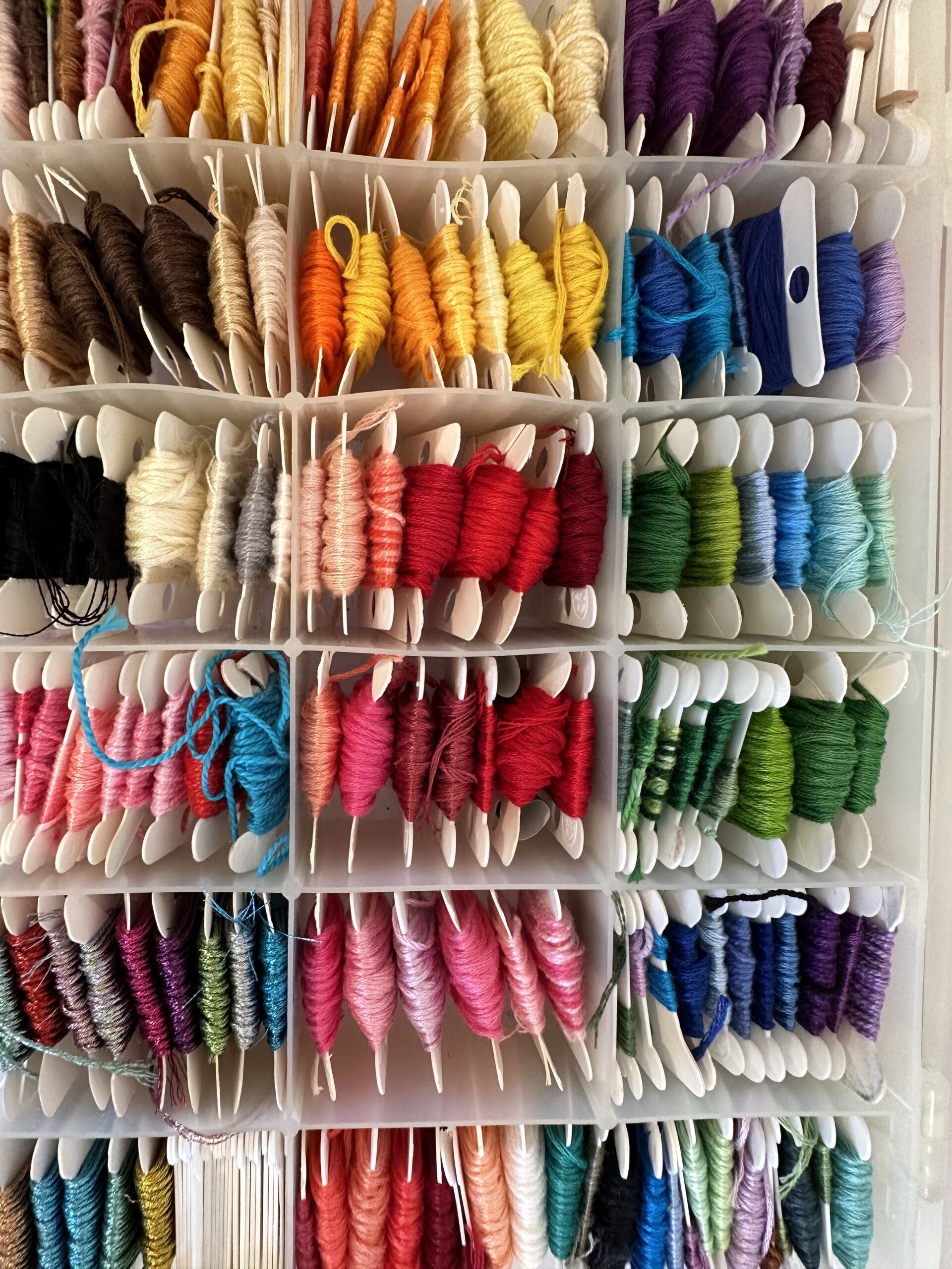 Overhead of a embroidery floss organizational tray with different colors of wound floss on bobbins